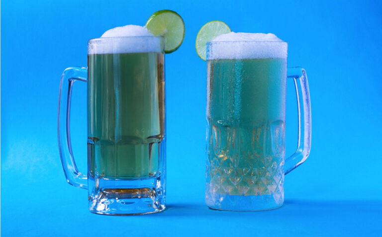 Dos tarros de cerveza con espuma y decorados con rodajas de limón. Uno presenta condensación y el otro no.