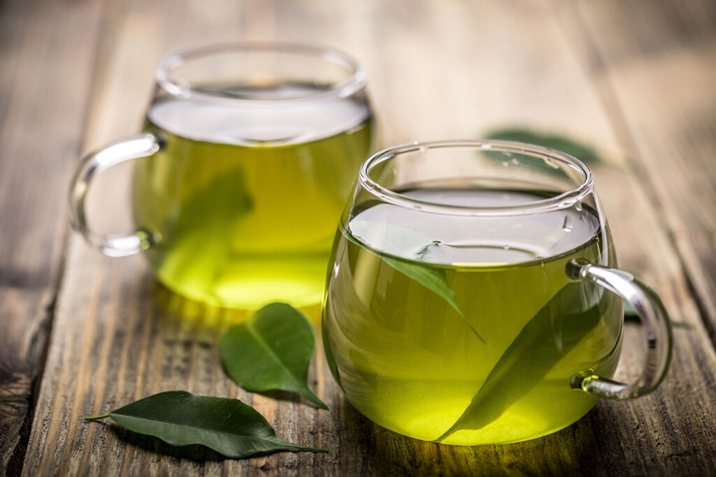Dos tazas de té verde y hojas de limón sobre una tabla de madera